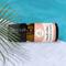 Bottle of Beach Vibes Essential Oil Blend on pool deck with palm fronds in the foreground and cool blue pool water in the background.